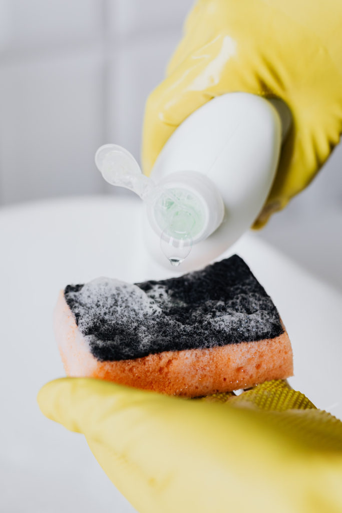 A gloved hand puts dish soap on a sponge to get ready to clean a bird feeder. 