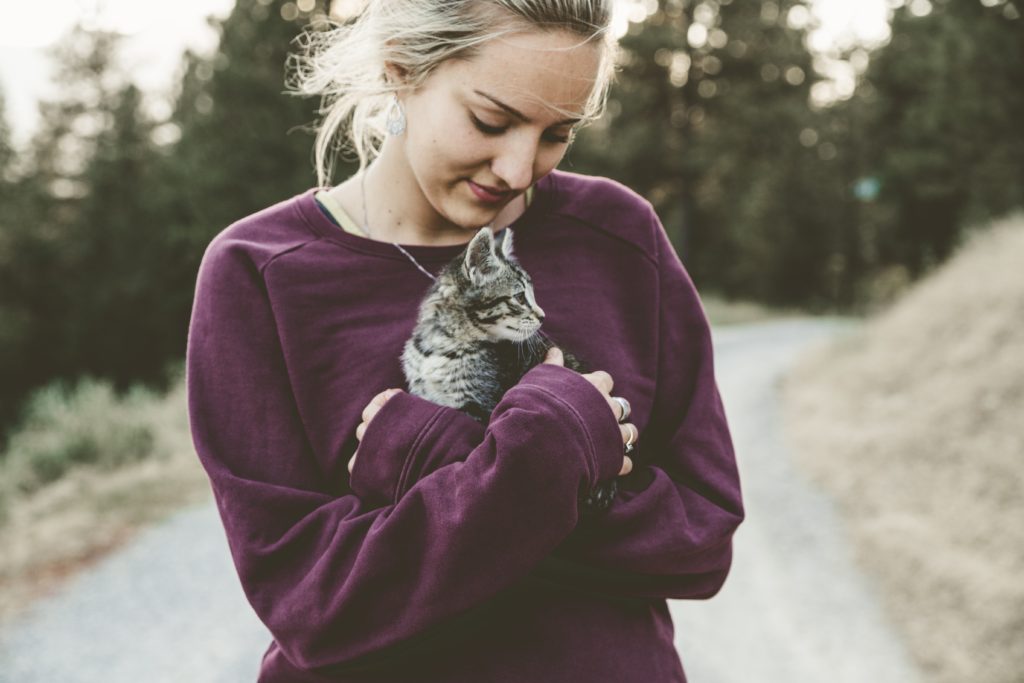 Woman holds her cat in her arms while walking outside on a trail.