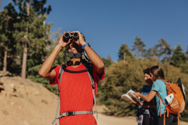 bird watcher wearing a red shirt, holding up binoculars looking for birds