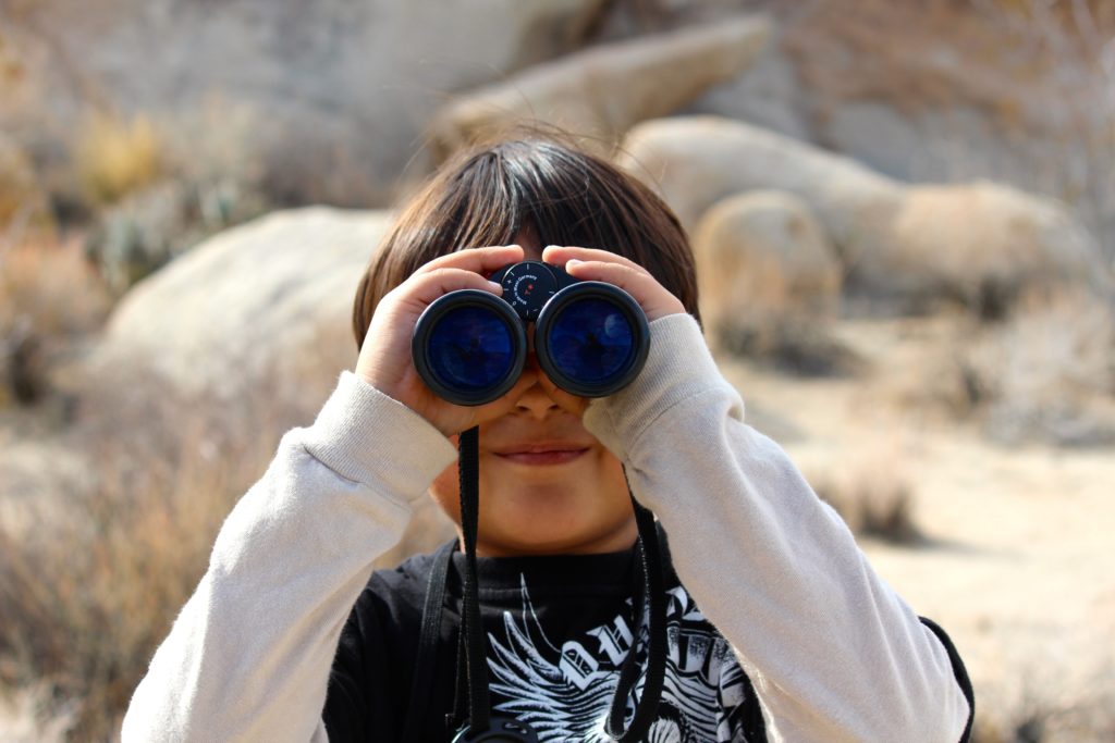 A boy looks through binoculars out in nature.