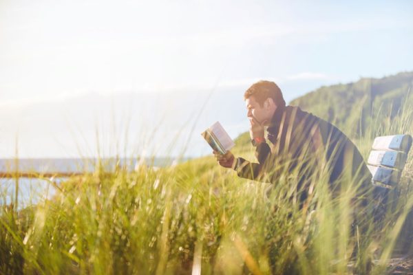 Man sitting on a bench in the wilderness, reading a book.
