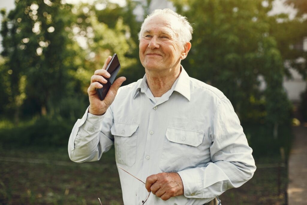 An smiling older man holds his smartphone to catch bird sounds as he tries birding by ear with a mobile app.