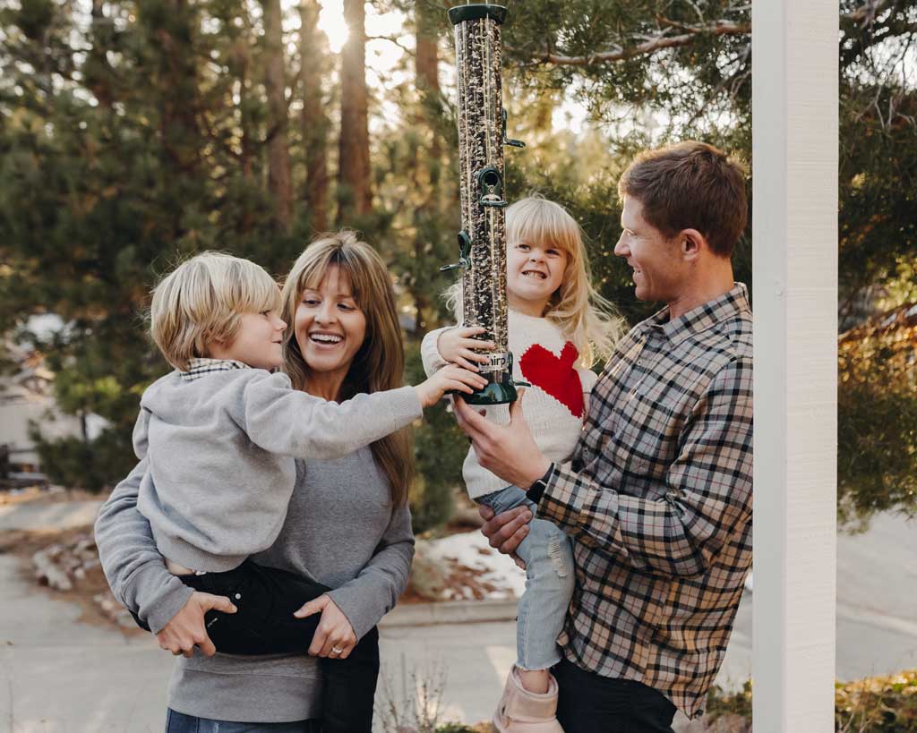 A couple with two young children hang a Chirp bird feeder together. 