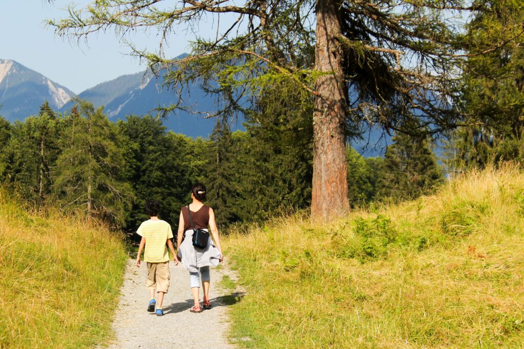 A mother and son hold hands as they walk down a mountain path.
