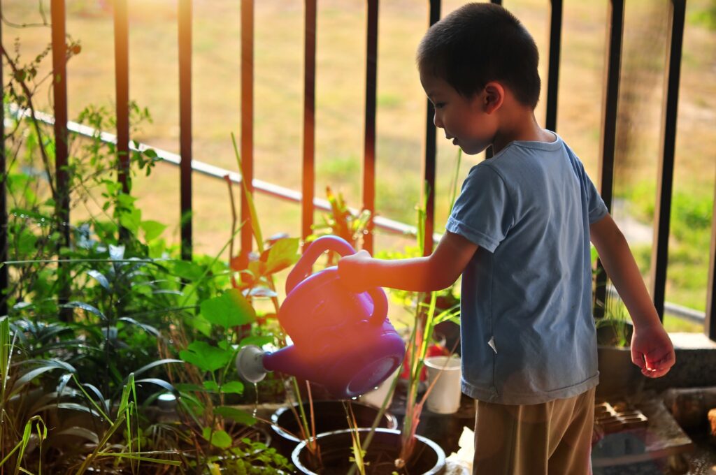A young boy waters potted plants in a backyard garden.