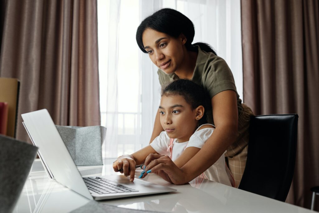 A mother helps her daughter on the laptop.