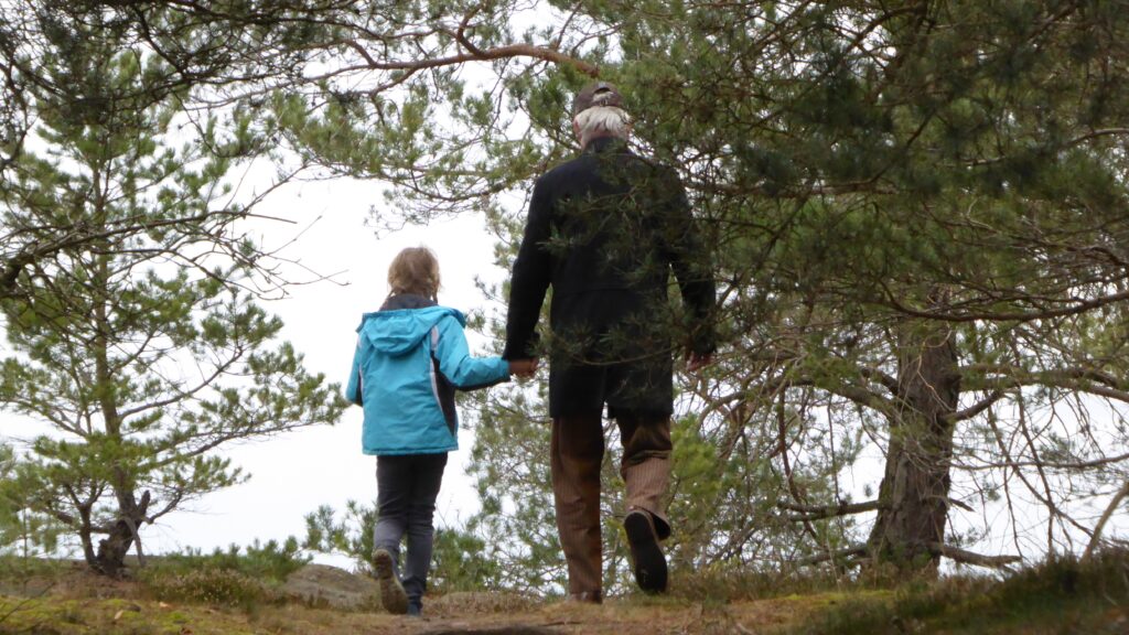 A man and his granddaughter walk hand in hand on a nature walk.