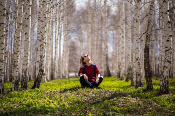 A smiling woman sits in a forest of aspen trees.