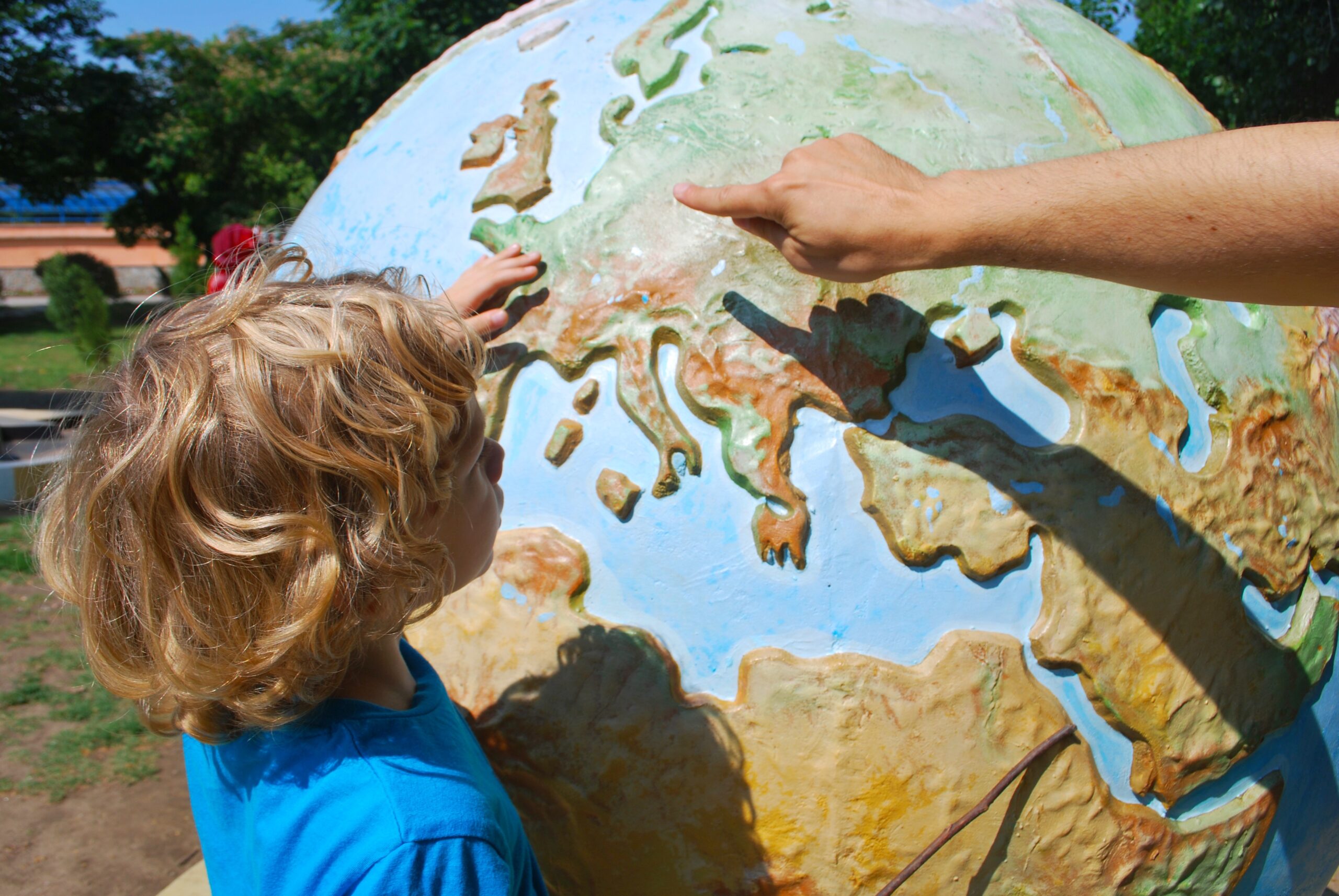 An adult points to a globe as a young boy watches.