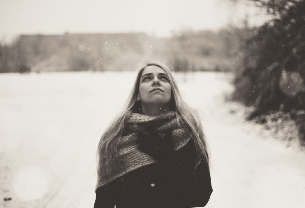 A woman stares into the sky with a sad expression while walking in the snow.