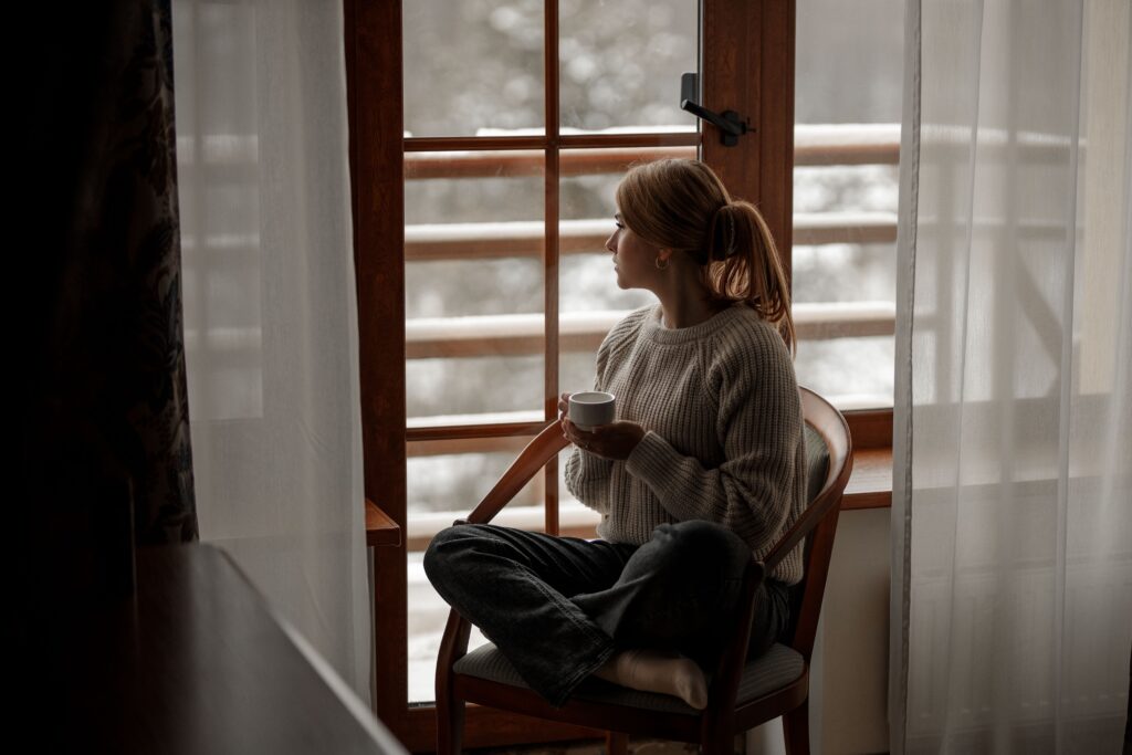 A woman gazes out the window at your bird feeder as the snow falls.