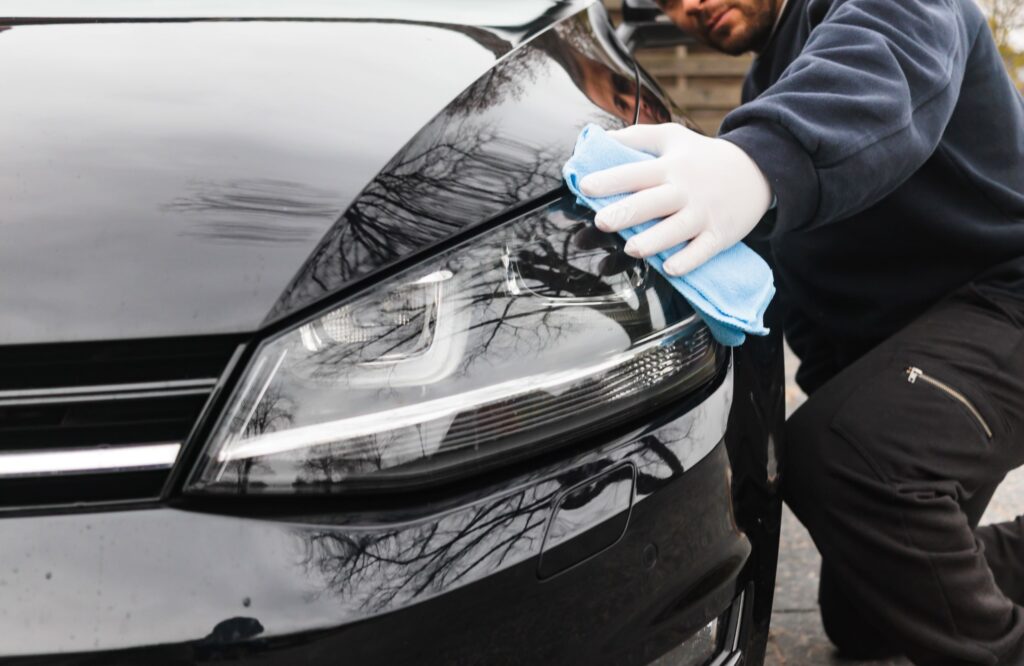 A man kneels down to clean the front side of his car with a microfiber cloth.