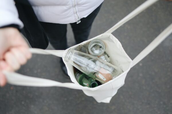 A woman carries a reusable cloth bag filled with glass jars to refill to live more sustainably.