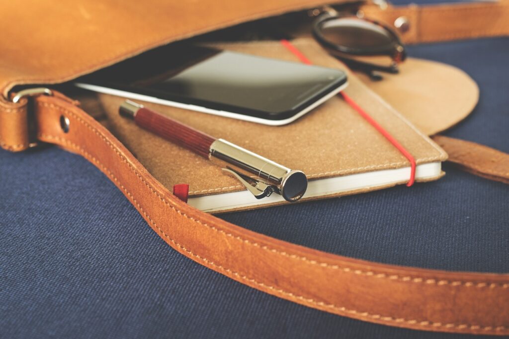 A leather bag with a smartphone, notebook, and pen. There are some tools you might use during the GBBC.