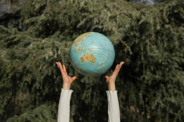 Two hands throw a globe in the air in front of a leafy background, in celebration of Earth Day.
