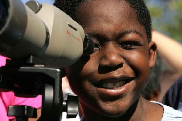 A young boy smiles as he peers through a pair of binoculars to look for birds.