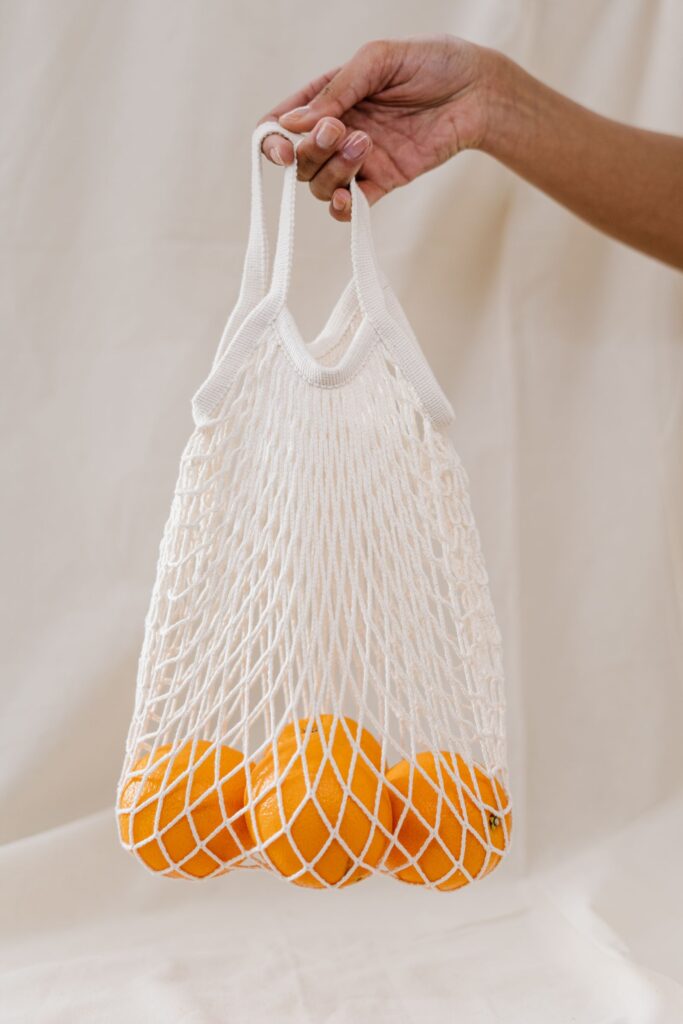 A hand holds an earth-friendly reusable mesh shopping bag filled with oranges.