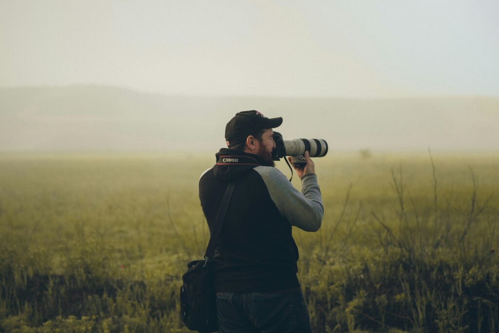 A man in a field uses a camera with a long lens to capture bird photos in the soft morning light.