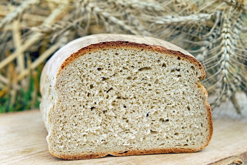 A loaf of bread, shown cut open, with wheat in the background. 