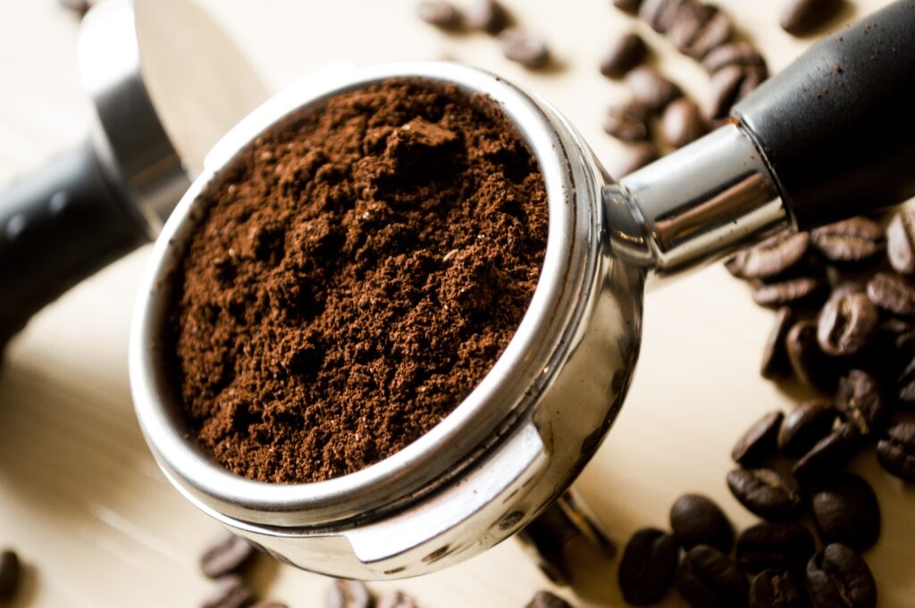 Fresh coffee grounds that are about to be brewed; coffee beans strewn in the background.