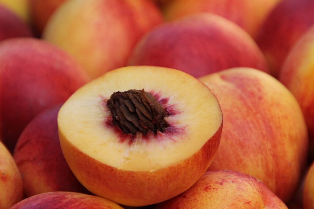 A peach, halved, with the pit shown, on a pile of peaches.