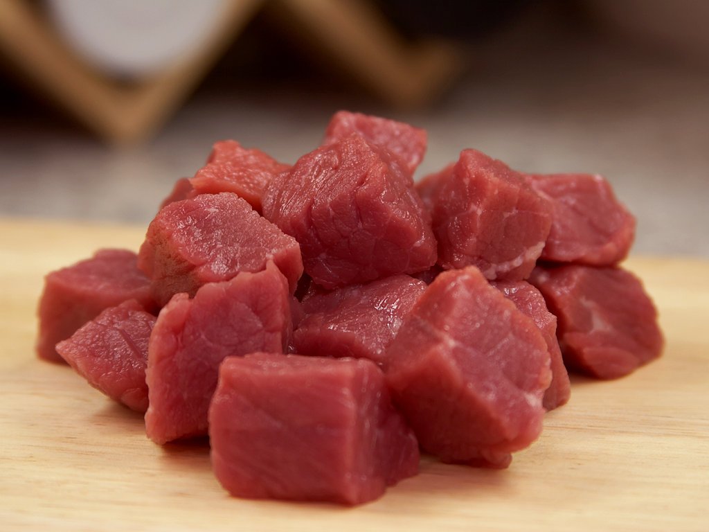 A pile of raw meat, sliced and cubed, on a butcher block.