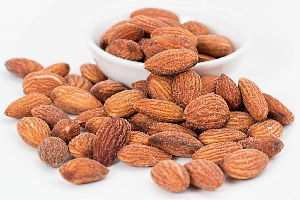 A small, white bowl of salted almonds overflows onto a white tablecloth.