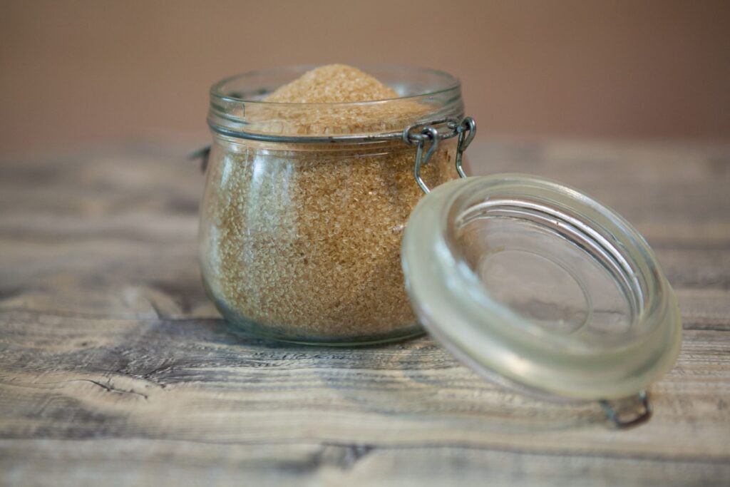 An open glass container of light brown sugar on a wood tabletop.