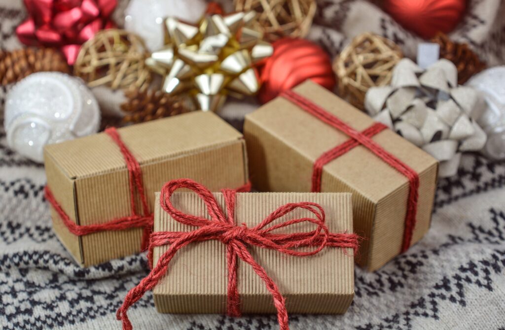 Recycled brown paper holiday boxes wrapped with red ribbon on a winter-white-themed background.