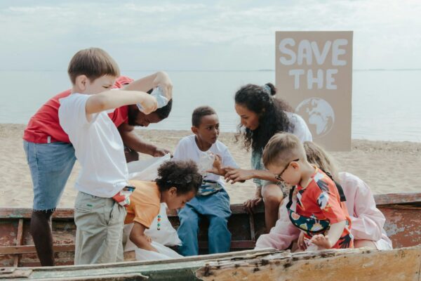 Three adults and four children gather together on the beach to pick up trash, a "Save the Planet" sign in the background.