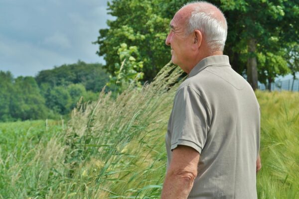 An older man smiles as he peers across a verdant natural landscape.