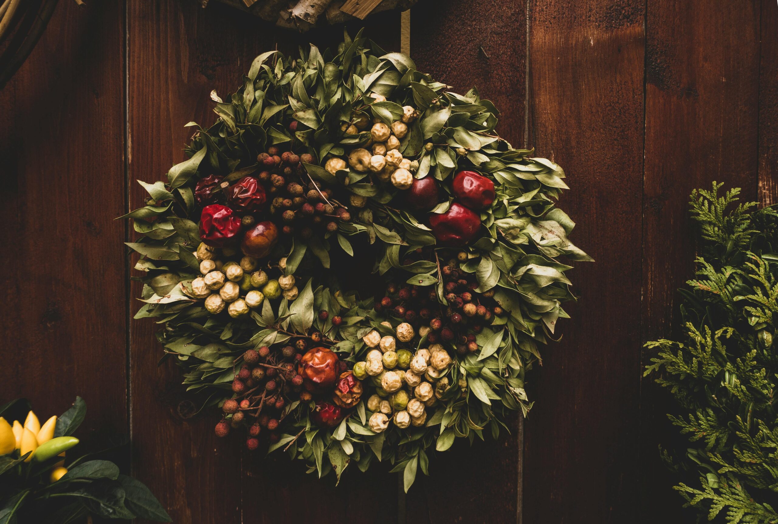 A gorgeous, natural wreath with greenery, fruits, and nuts on a dark-stained wood door.