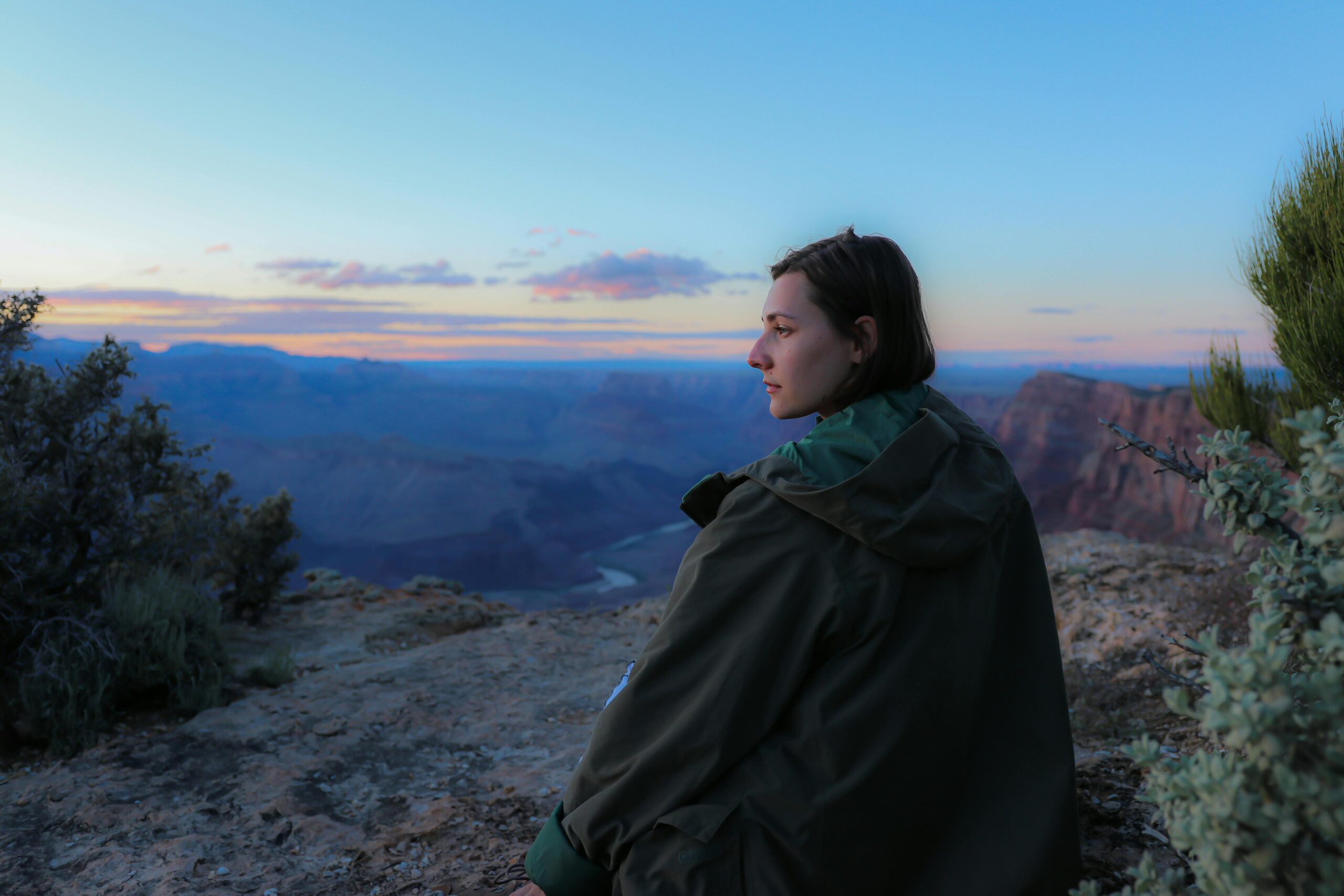 A teenage girl stairs out peacefully at a beautiful sunset in a serene mountain setting.