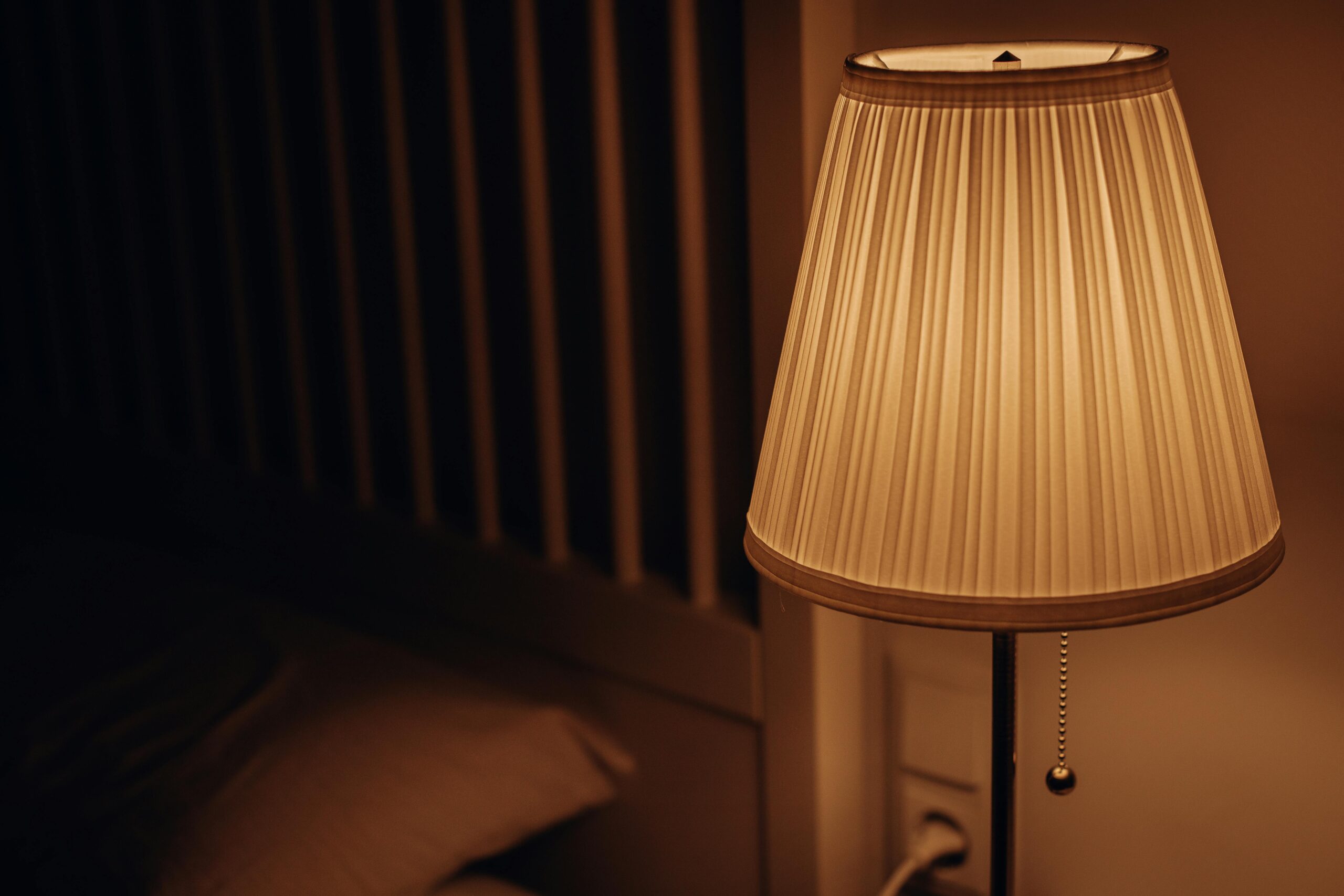 A dimmed bedside lamp glows faintly next to a bed.