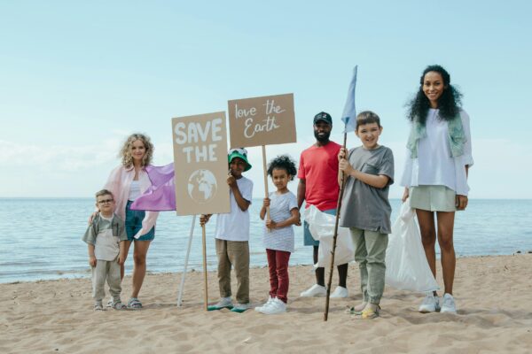 A mixed-race family of two adults and three children of varying ages stand on the beach holding "save the earth" signs while smiling at the camera.
